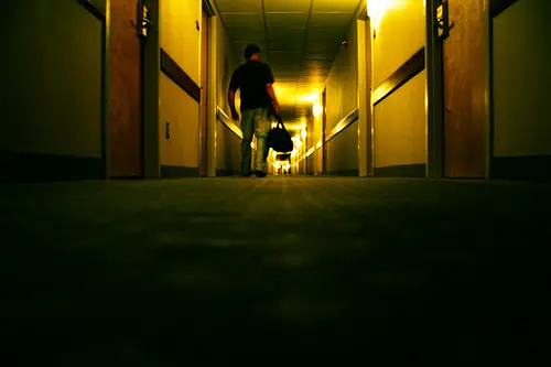 Man_with_bag_in_dark_hotel_corridor 