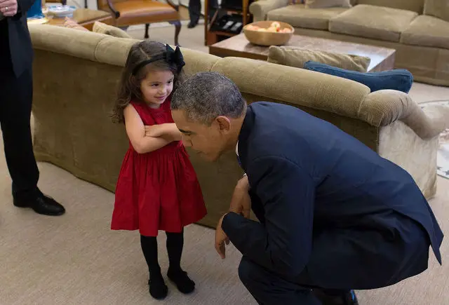 President Barack Obama bends down to listen to the daughter of a departing U.S. Secret Service agent in the Oval Office, Oct. 28, 2013.