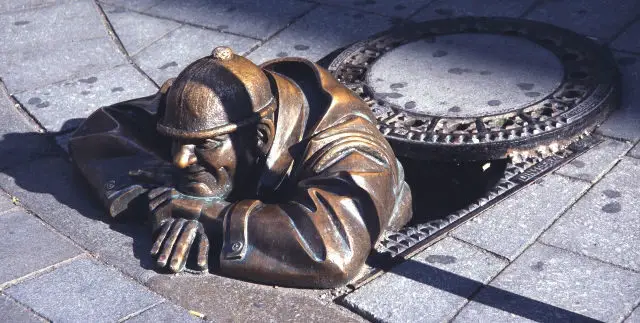 sculpture climbing out of manhole 