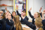 pupils in a classroom with their hands up