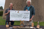 Sandra and Ian Graham holding giant cheque with display of items made on table in front of windmill