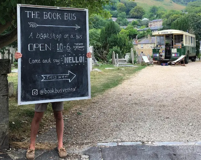 Tom holding chalk board sign pointing to the Book Bus