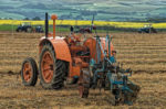 Vintage tractor in field with other tractors working in distance