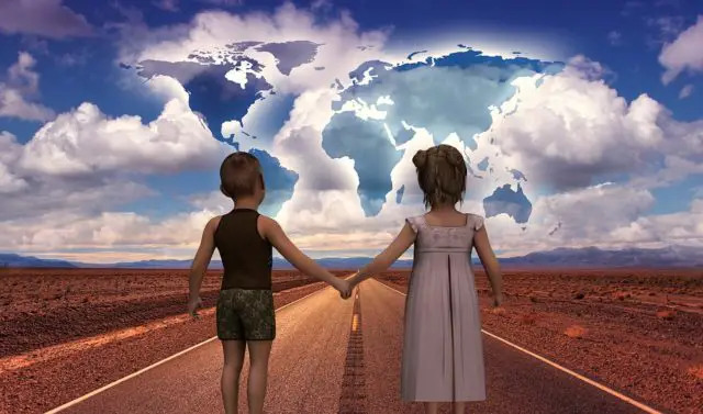 Two children looking ahead on road with world map in the clouds