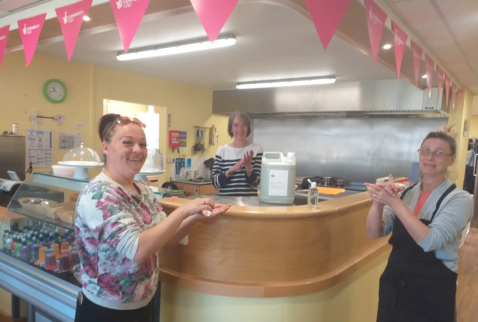 Kirsty Gwilliam (Café Assistant); Rachel Thomson (Community Centre Manager); and Wendy Parsons (Café Supervisor) - and a five litre 'flagon' of the hand sanitiser at the centre which is labelled 'True Island Spirit'