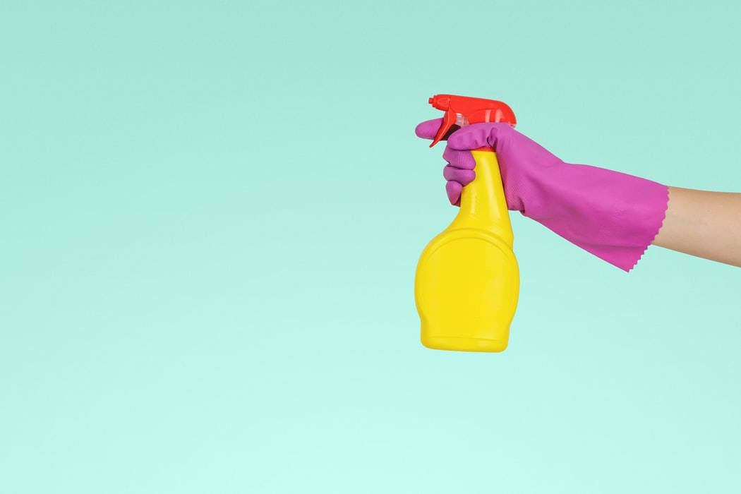 Person with rubber gloves holding a spray bottle of household cleaner