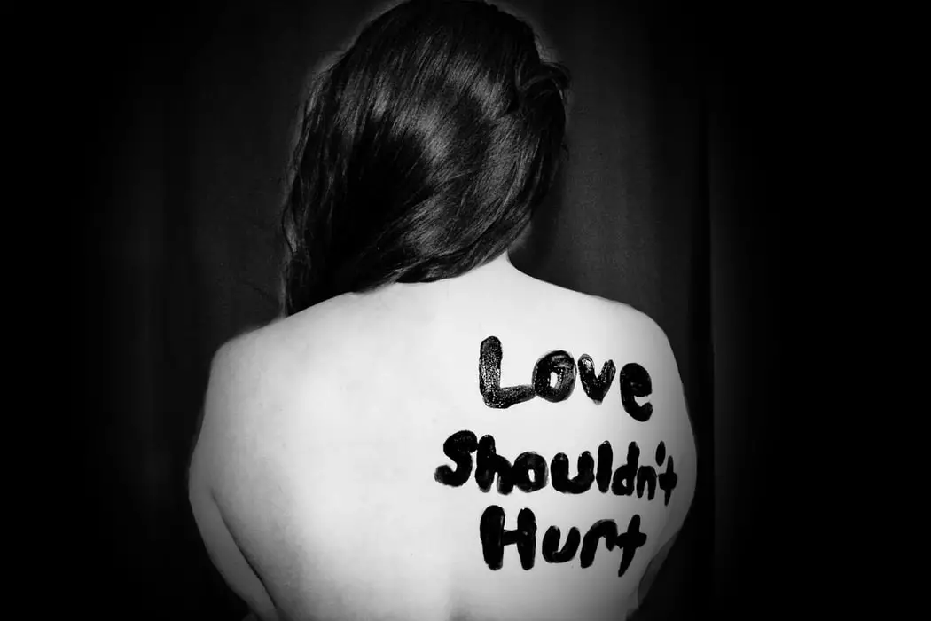 love shouldn't hurt written on bare back of woman