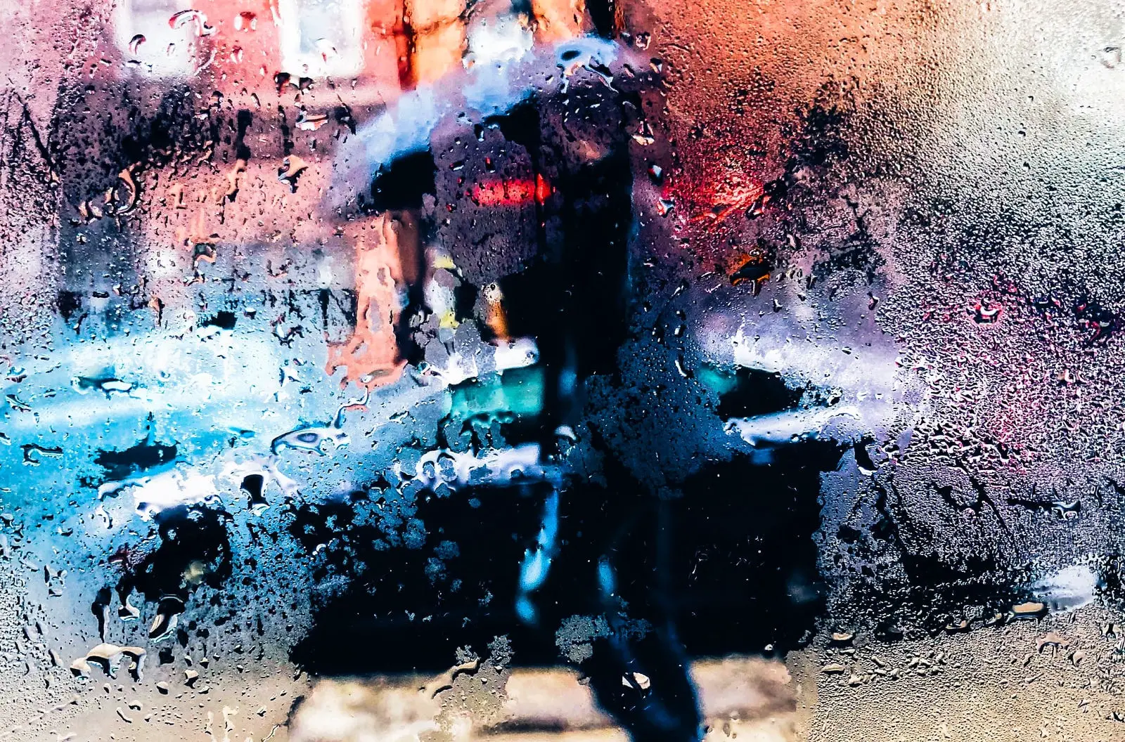 person with umbrella in the rain through a window