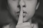 Woman with finger over mouth signalling a shh