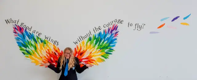 Athiea Mitchell standing against the mural - what good are wings without the courage to fly