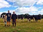 Three generations of the Holliday family standing in a field with their dairy cows
