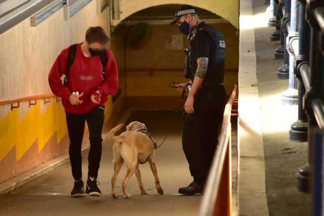 British Transport police with dog at entrance to train station tunnel with passing passenger