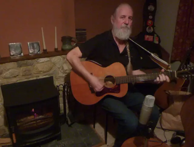 Andy Roberts by the Fireside with guitar in hand