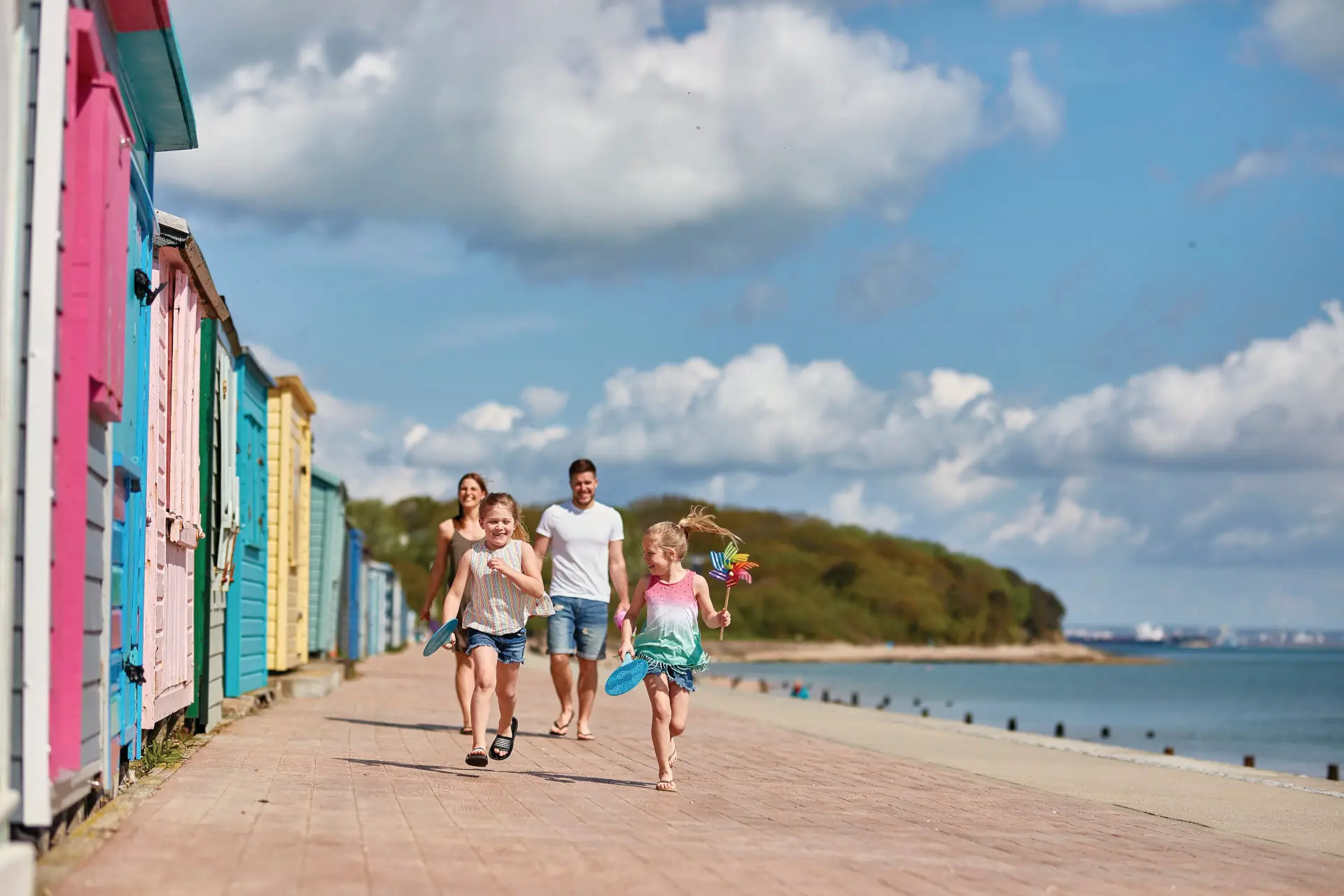 Children running along Nodes Point Beach past colourful beach huts