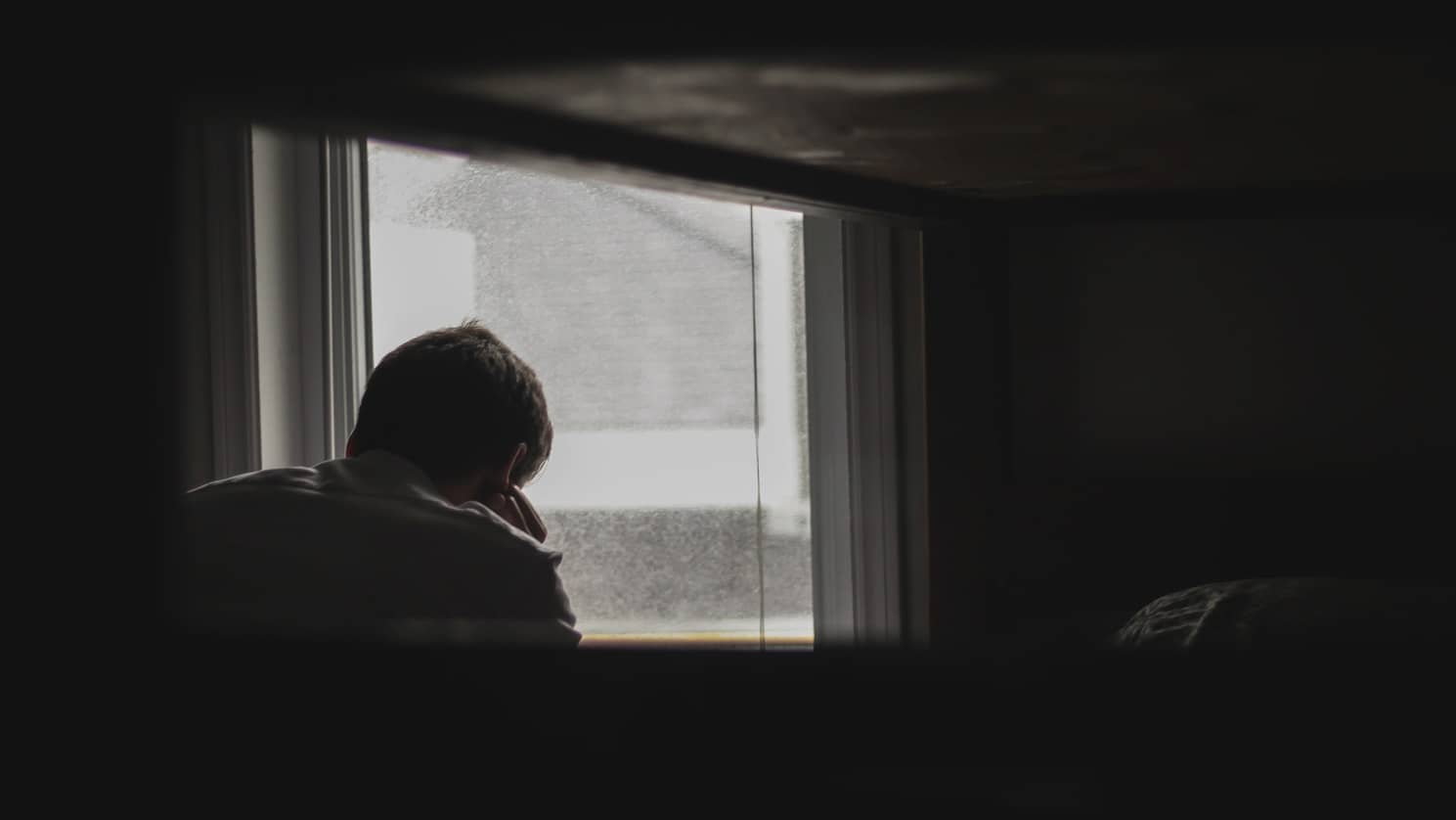 man looking depressed out of a window