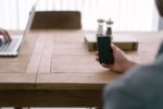 person using laptop at table and another holding a mobile phone - blurred