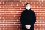 Man with mask standing against brick wall