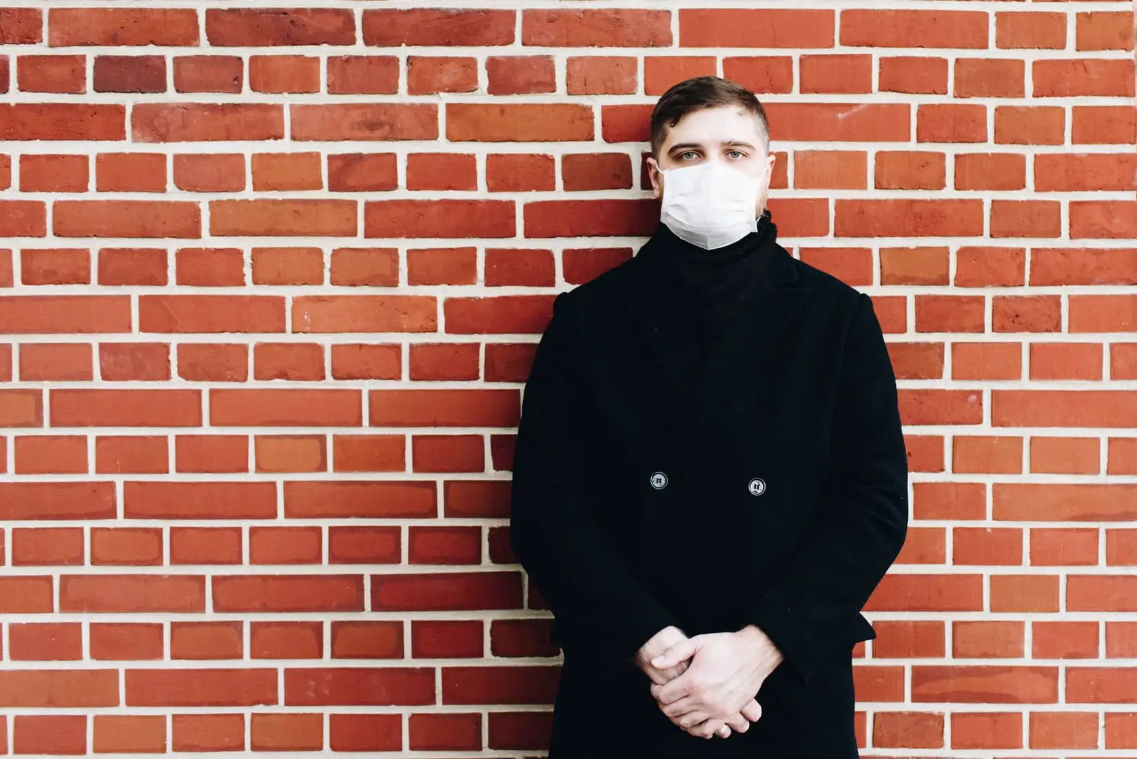 Man with mask standing against brick wall