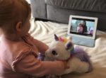 Baby watching a live facebook video on a laptop whilst holding a unicorn teddy
