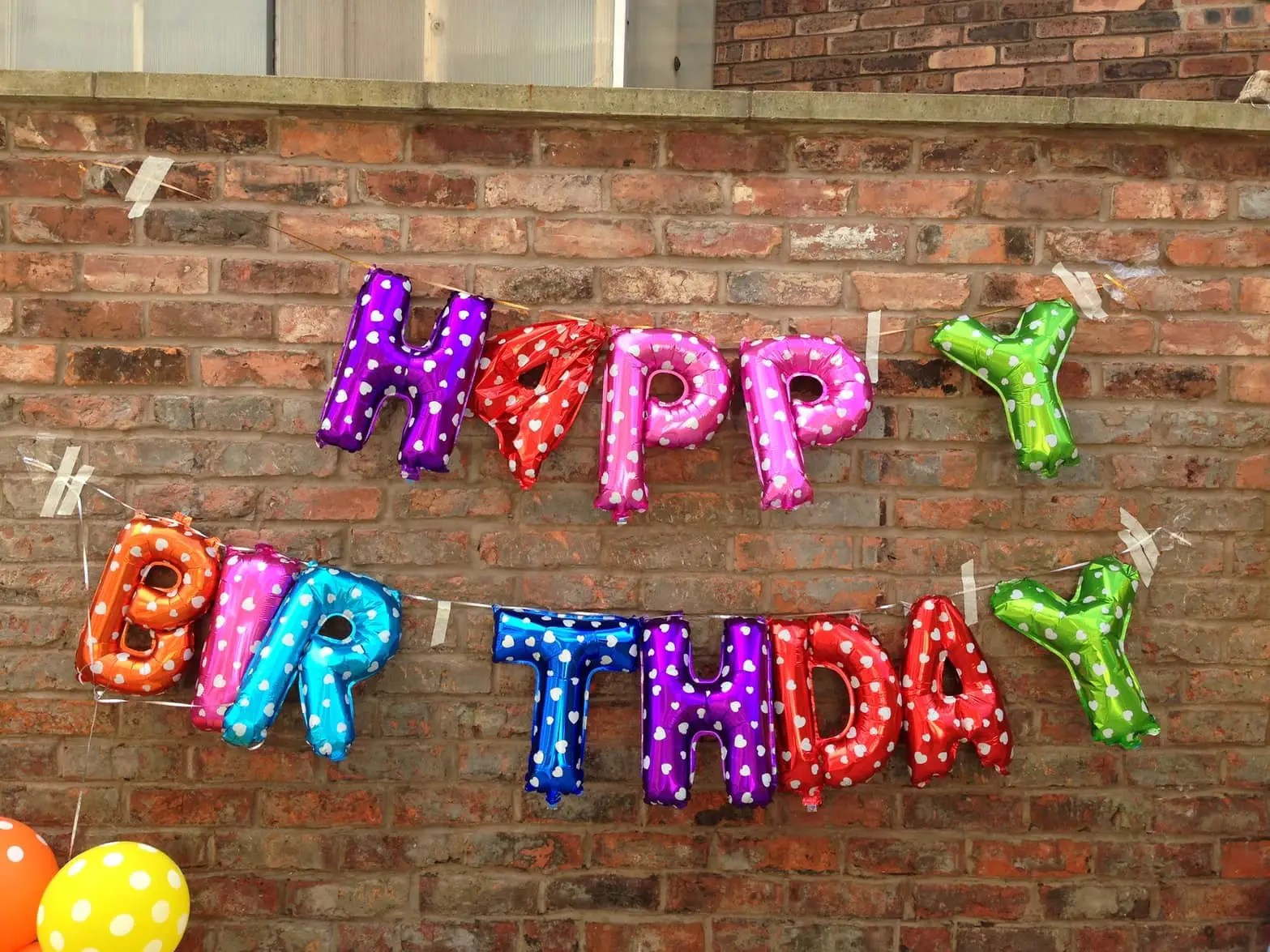 Happy birthday balloons hung from a brick wall