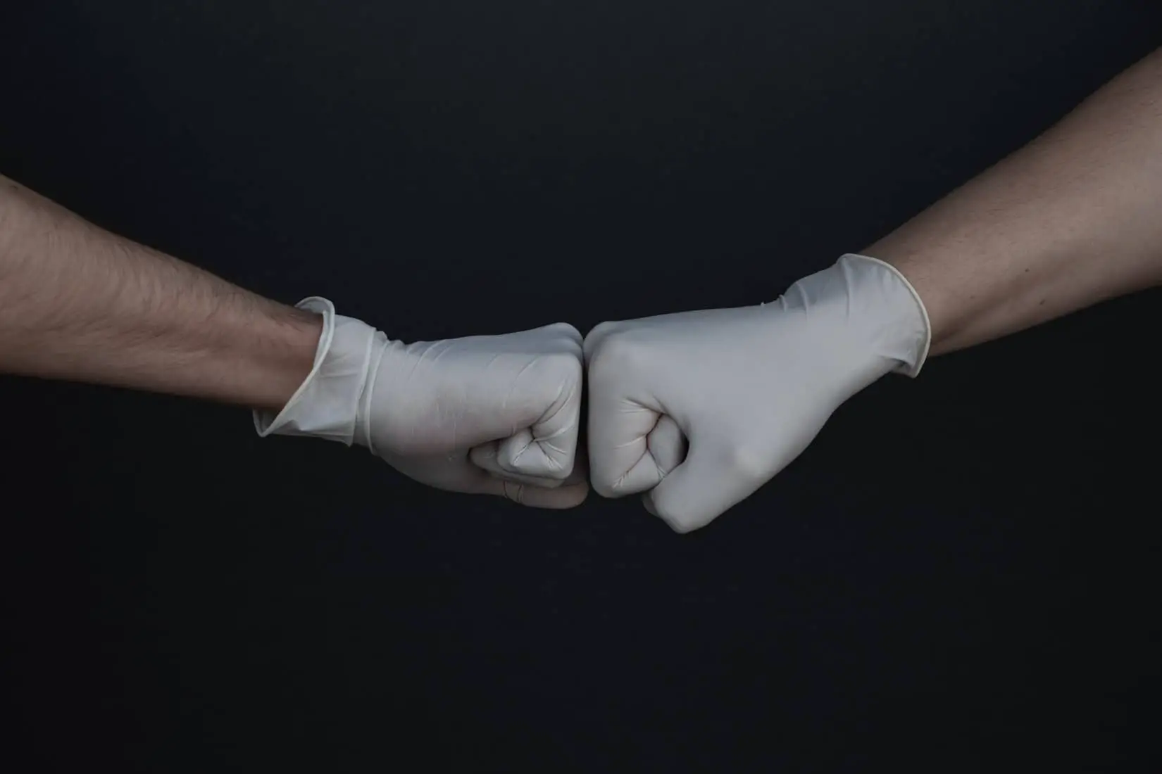 Two people with surgical gloves fist bumping