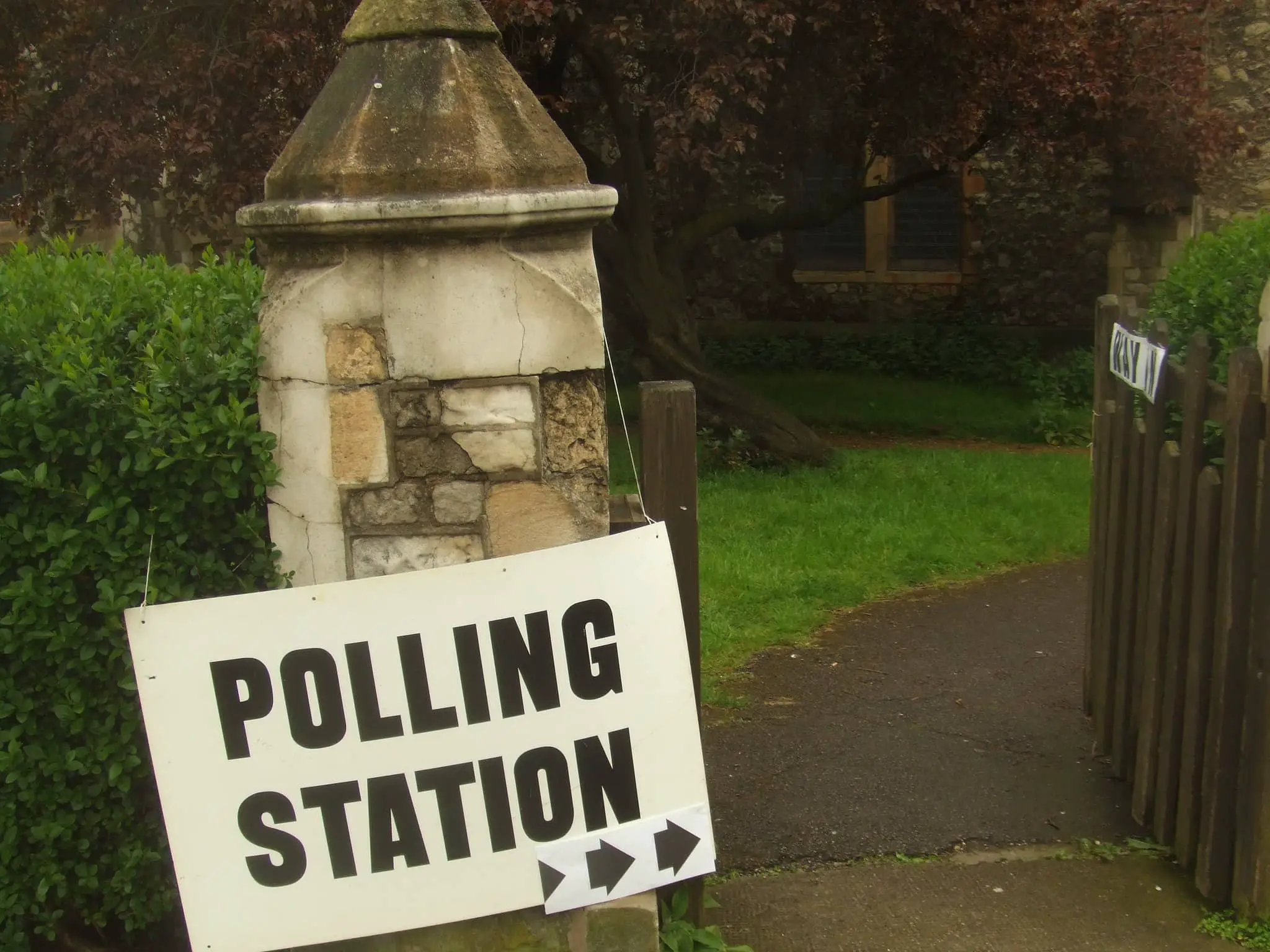 Polling station sign on wall leading into garden