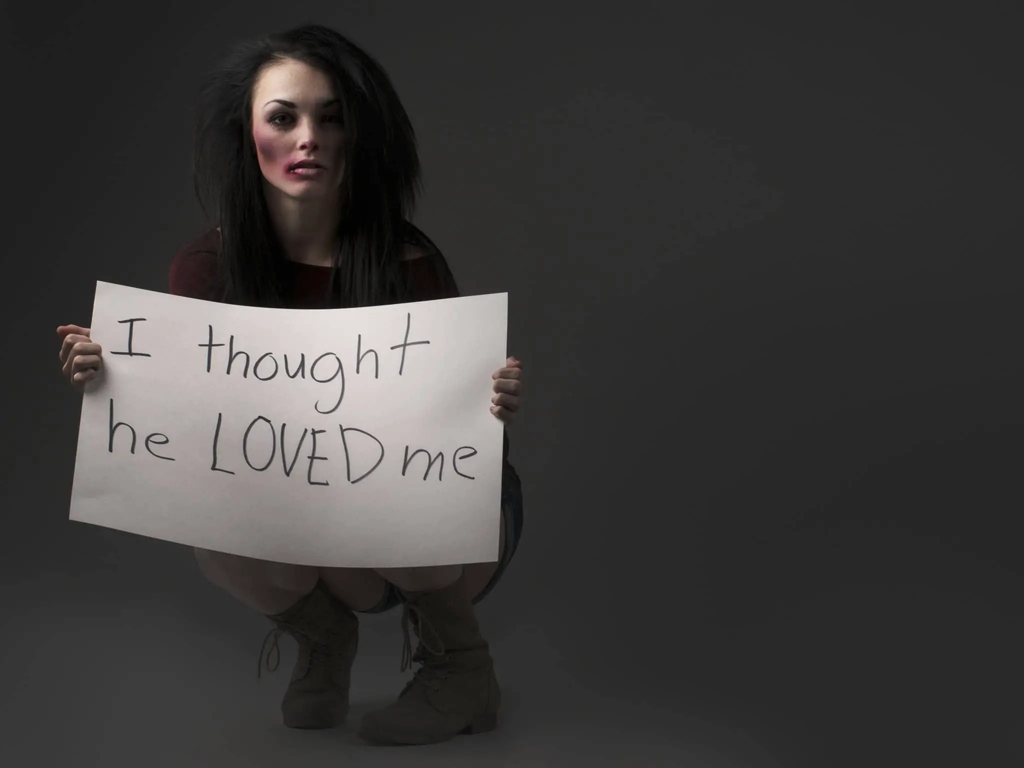 Woman kneeling down and holding a sign that says I thought he loved me