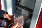 person putting twenty pound notes in wallet at cash machine by Nick Pampoukidis
