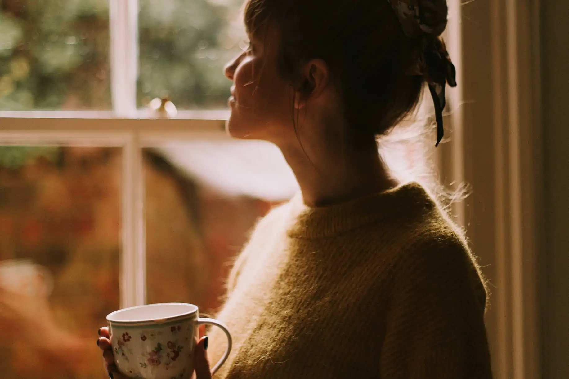 woman looking out of window holding a cup in her hands
