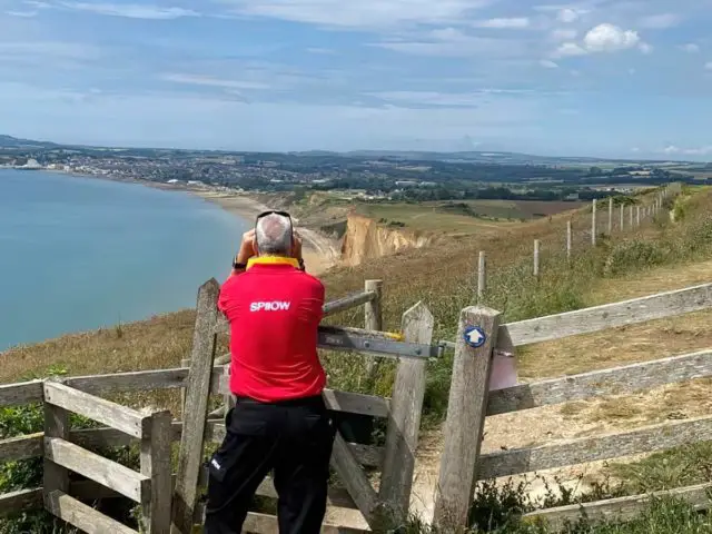 SPIIOW volunteer looking into bay with binoculars on cliff edge