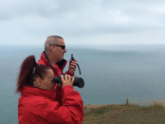 SPIIOW volunteers in red jackets standing on cliff edge with binocular