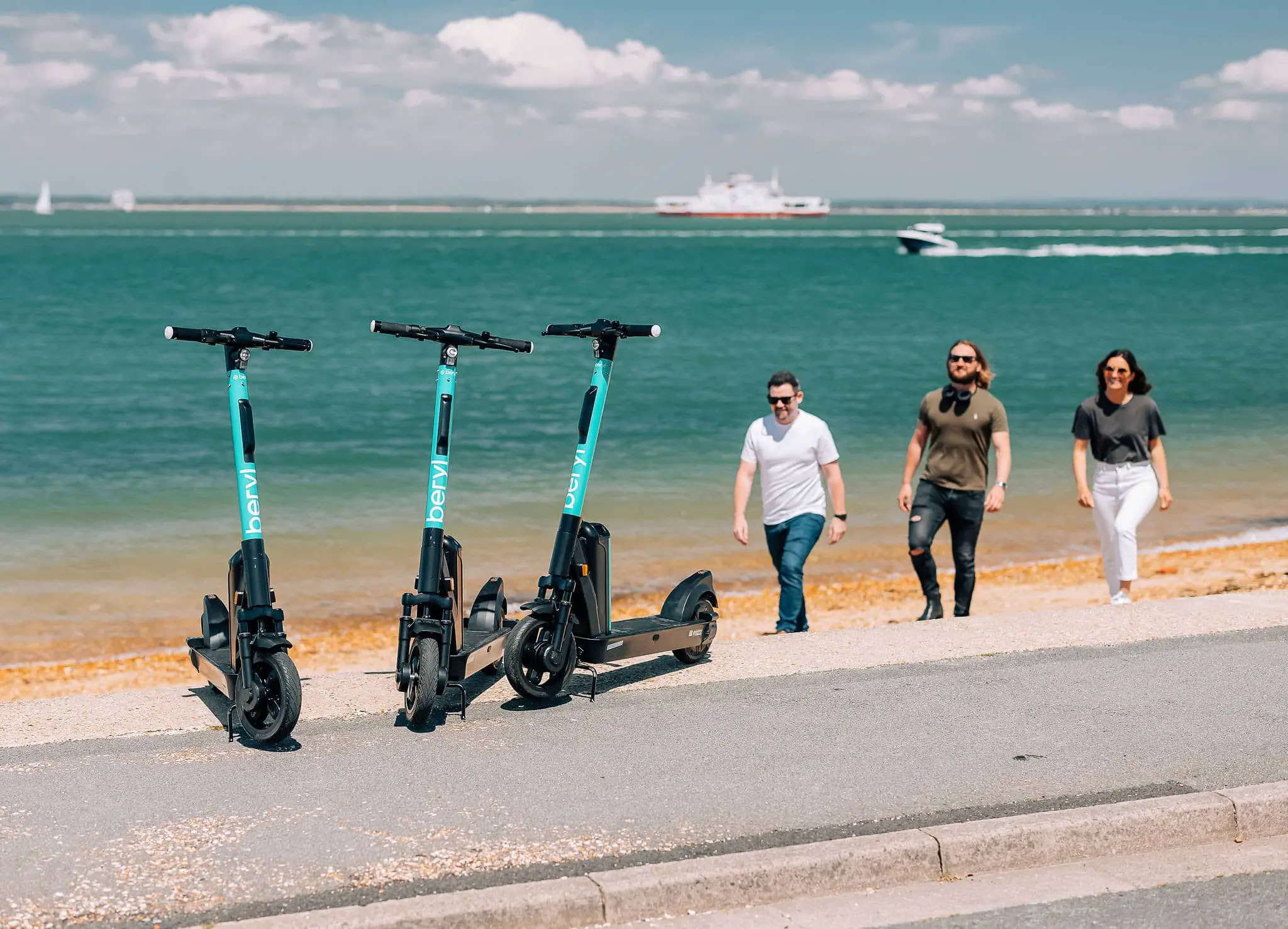 Beryl scooters on the seafront with three people walking towards them from the beach