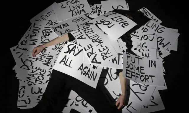 Man lying on floor large cards with writing on them covering him