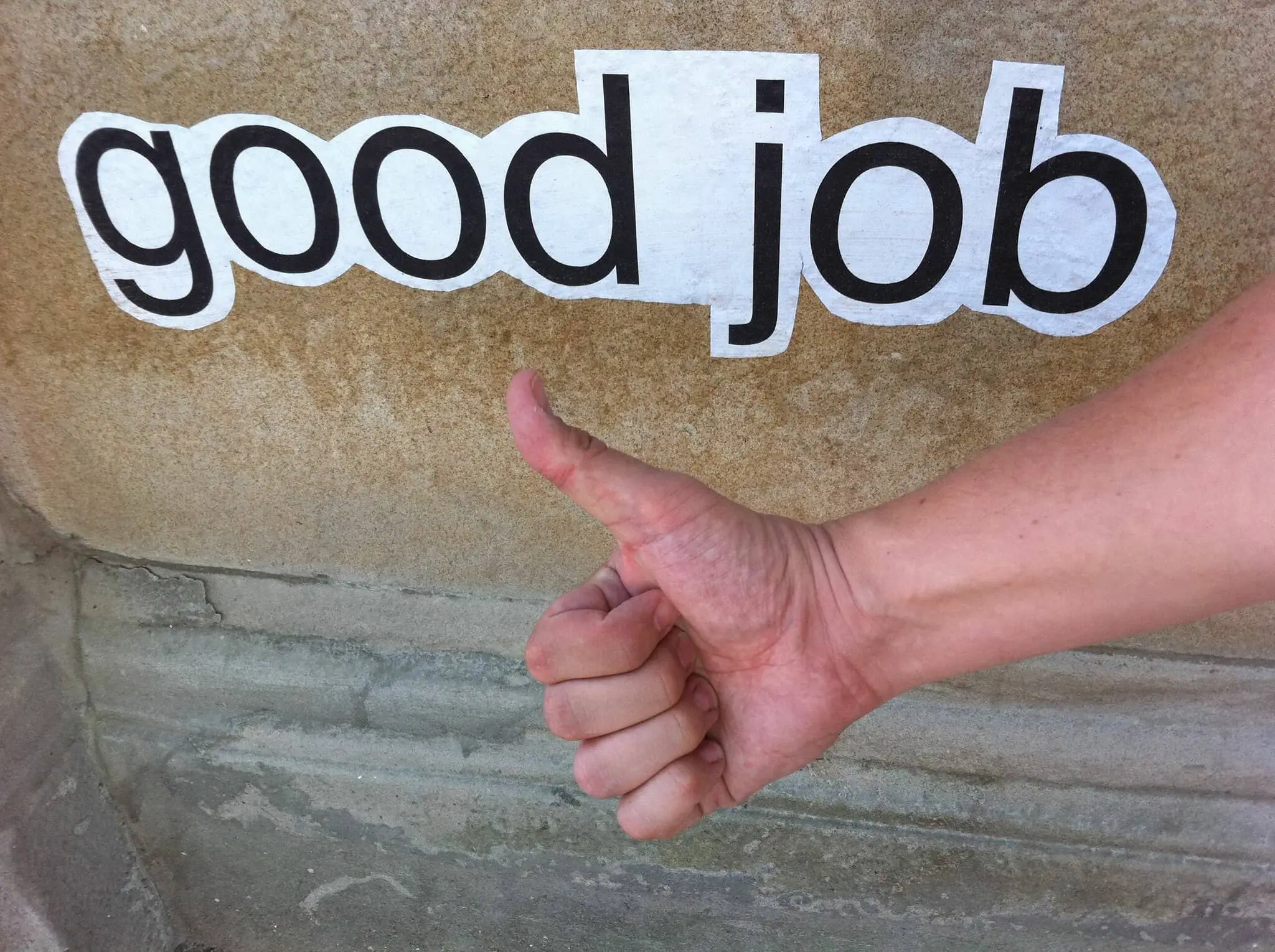 Sign reading good job and mans arm and hand giving thumbs up