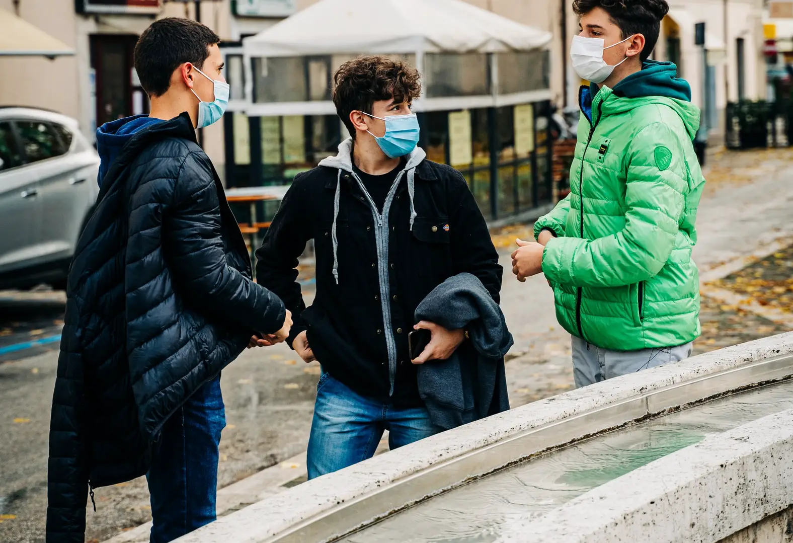 three teenage boys talking in the street and wearing masks