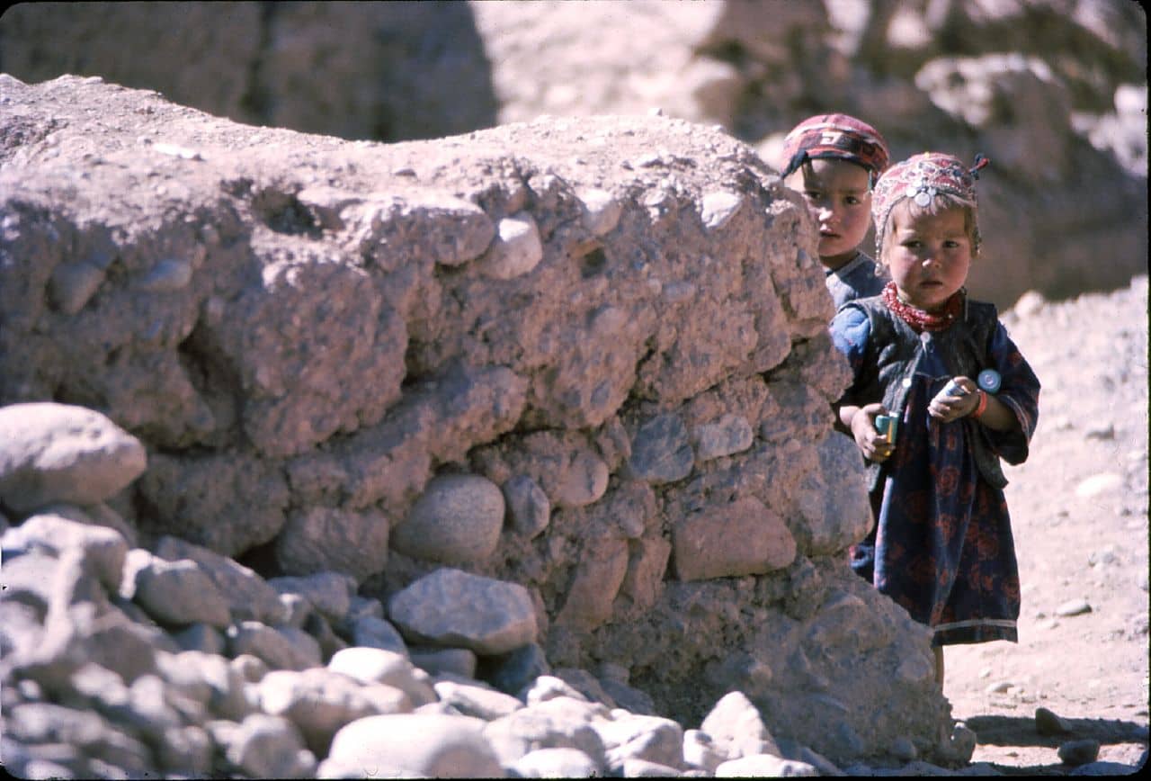 Two afghan children standing behind a wall