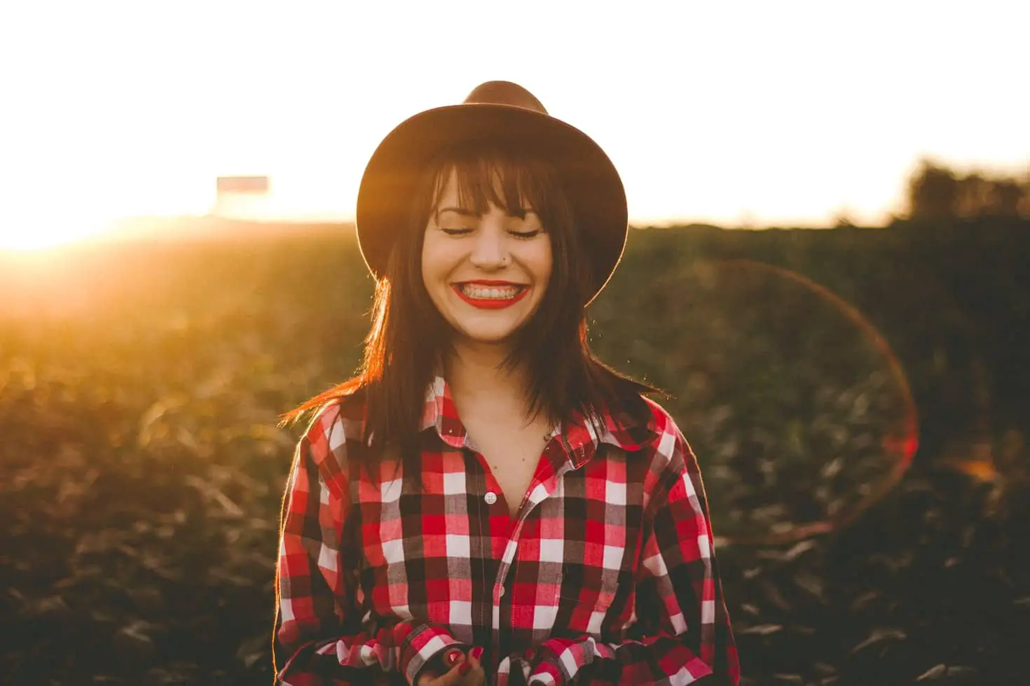 Woman standing in a field wearing a checked shirt and cowboy hat smiling