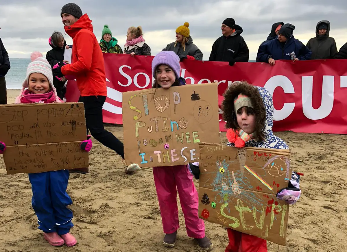Campaigners on the beach along with children holding stop the sewage signs