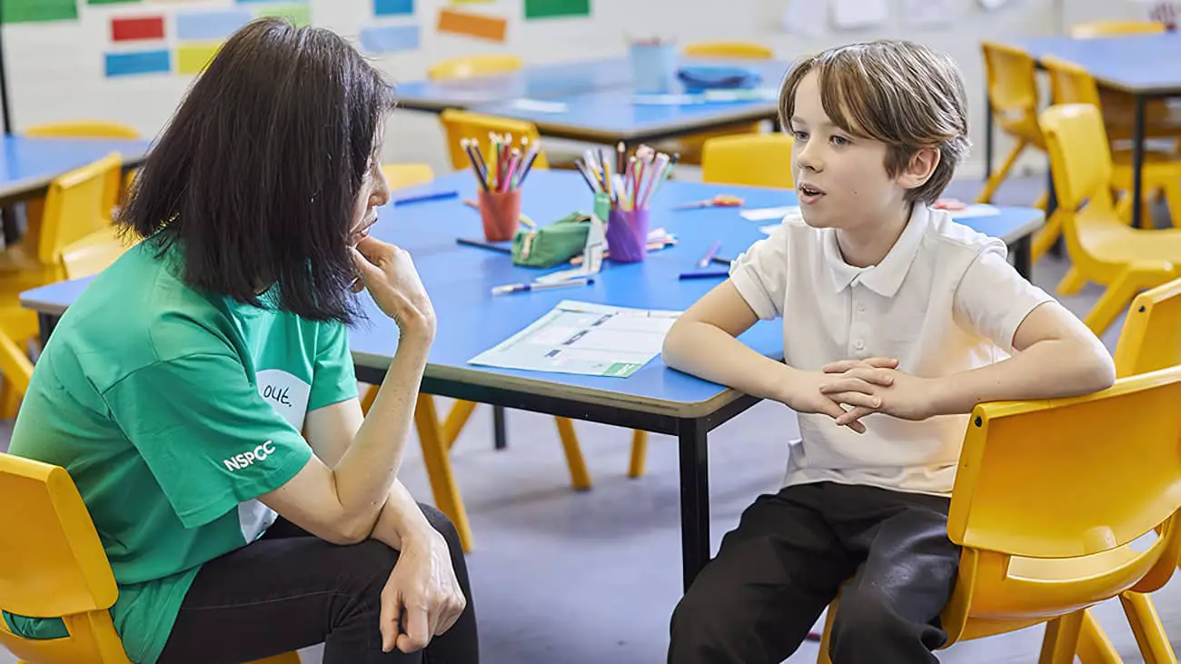 Child and nspcc member talking in classroom