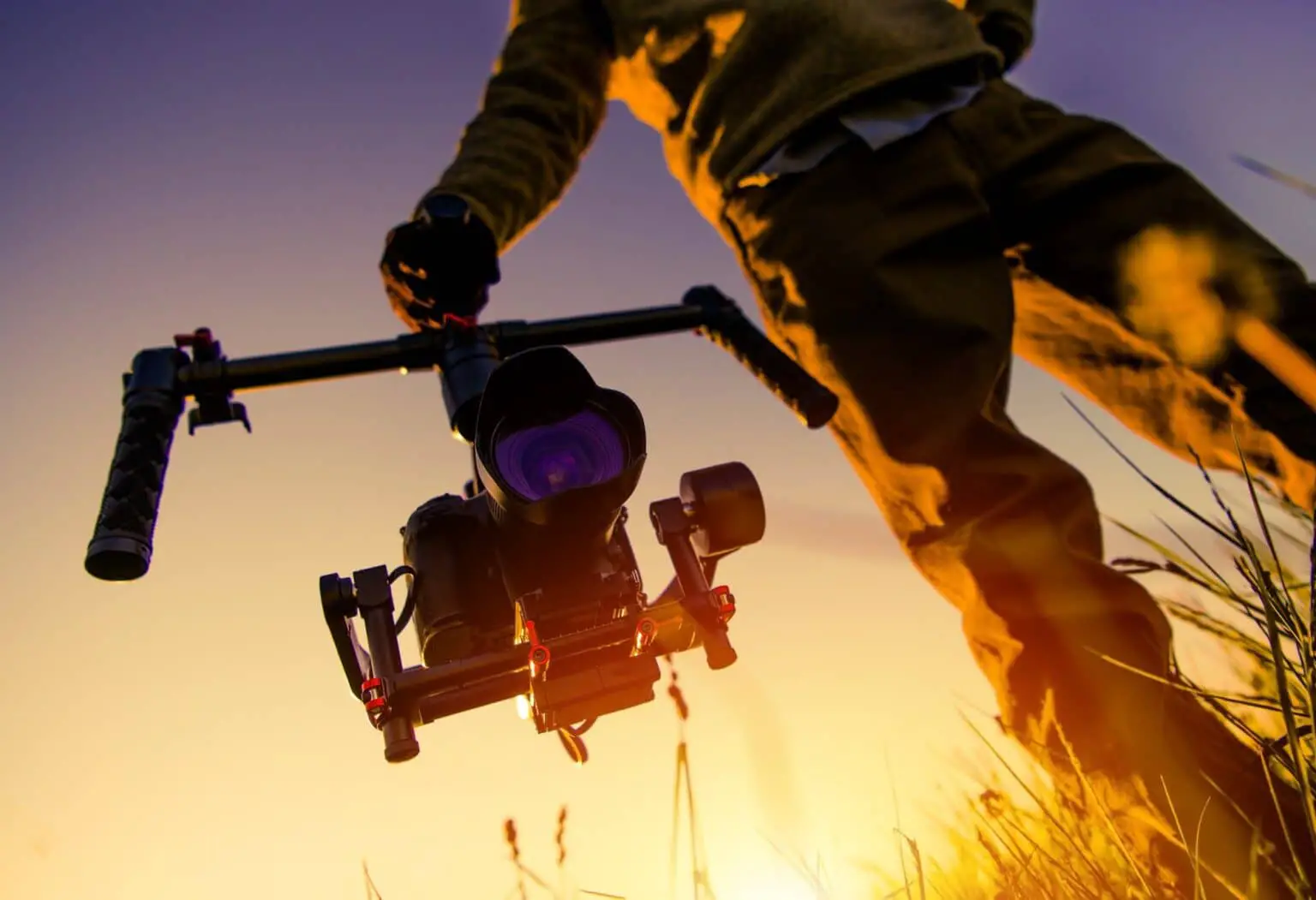 Person holding professional video camera low in the field with sun behind