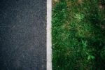 Half photo is asphalt road surface and other half is green verge
