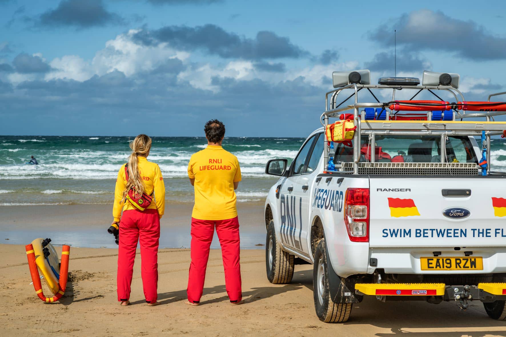 RNLI livesavers looking out to sea, standing next to a vehicle
