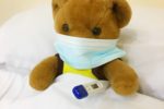 Teddy bear in bed with mask and thermometer