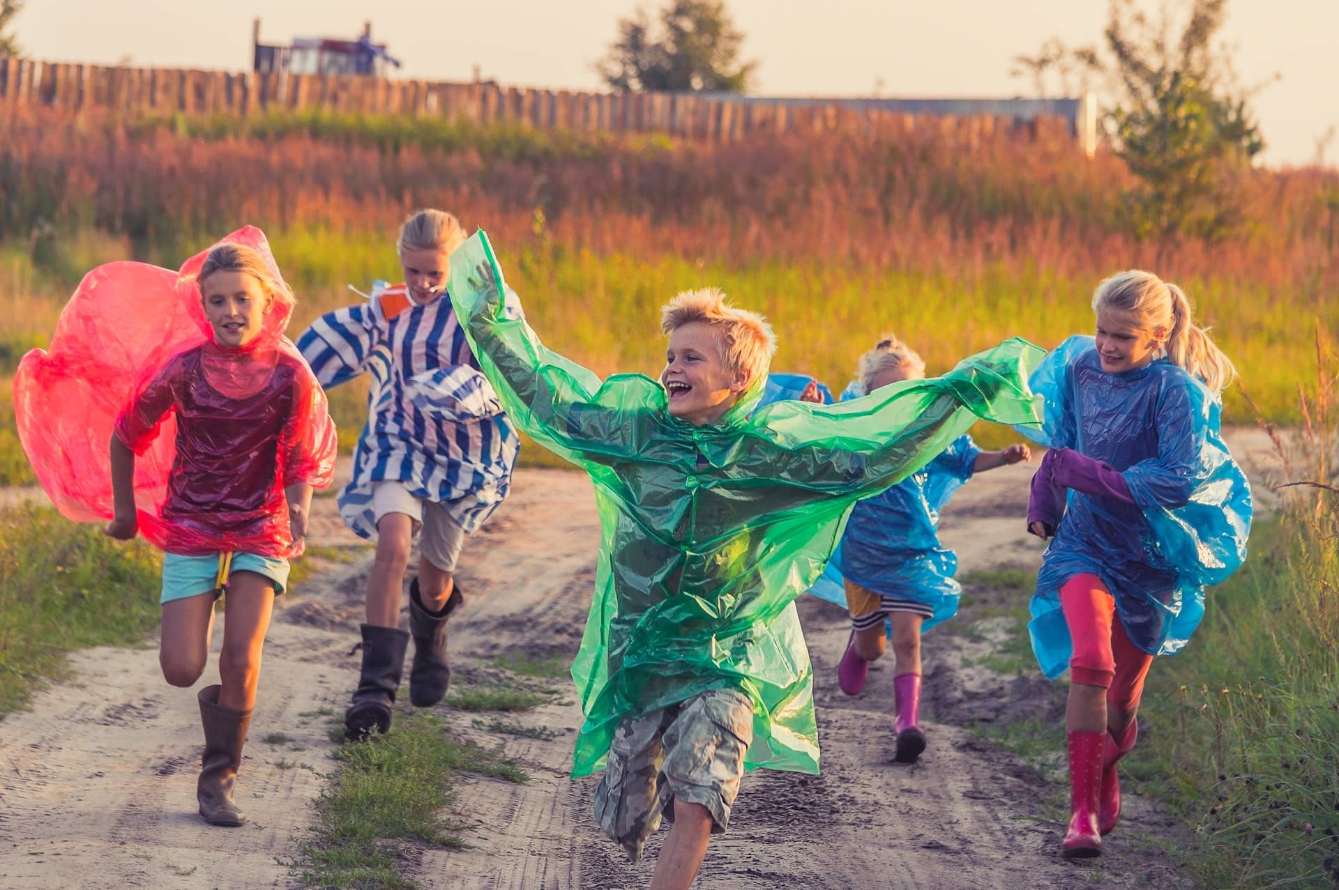 Children running in wellies and wearing rain macs