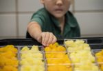 child selecting a portion of fruit in school canteen