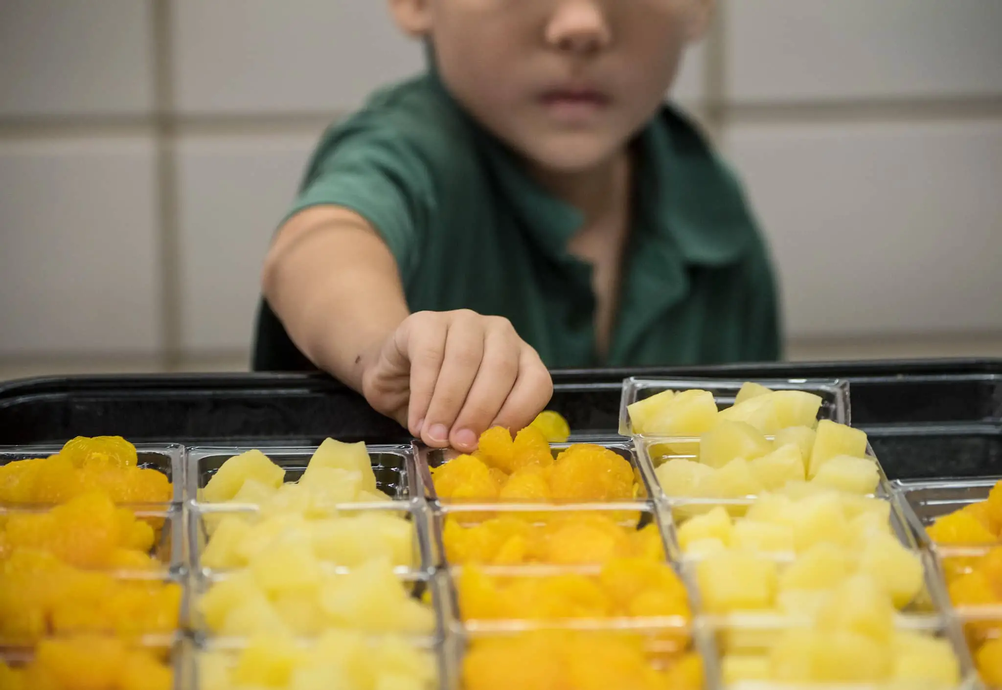 child selecting a portion of fruit in school canteen
