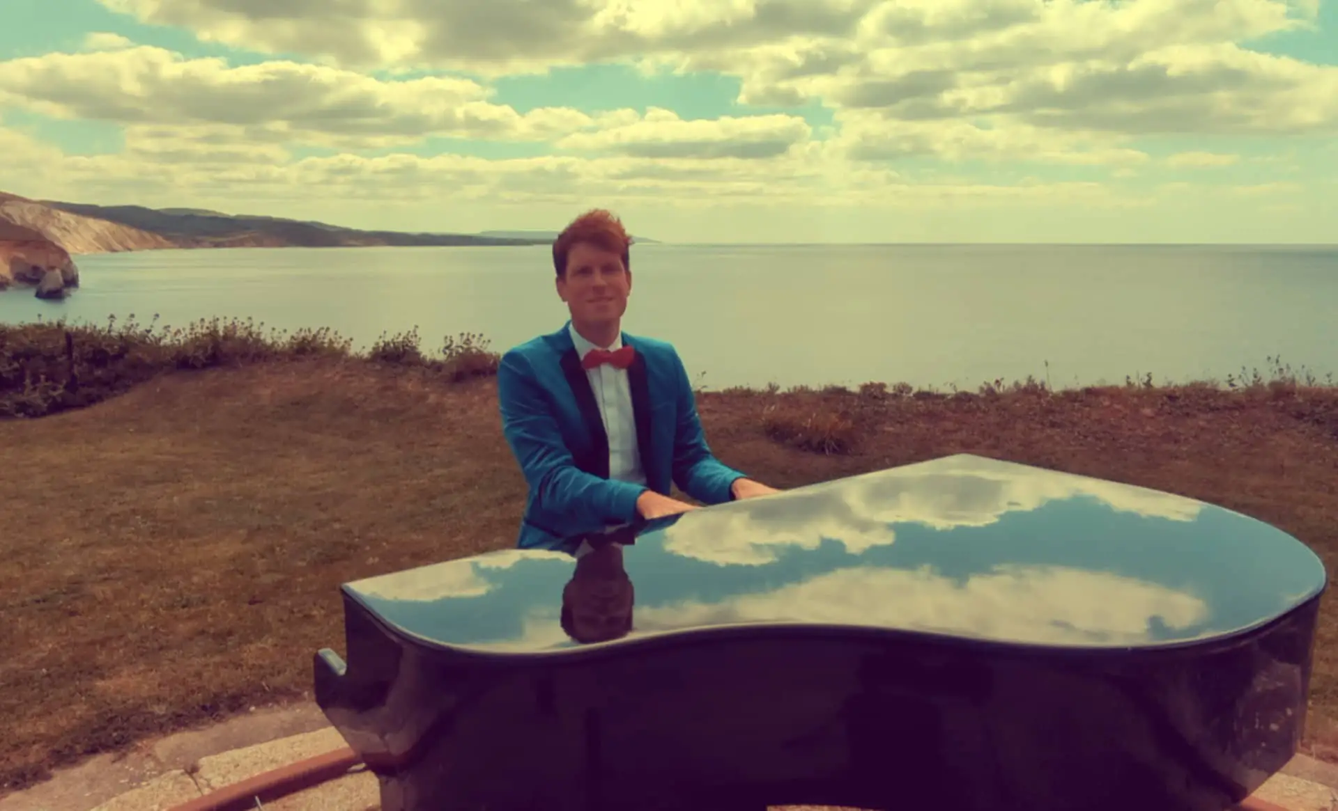 Mike playing the grand piano by cliff edge on Heartbeat of Our Nation video