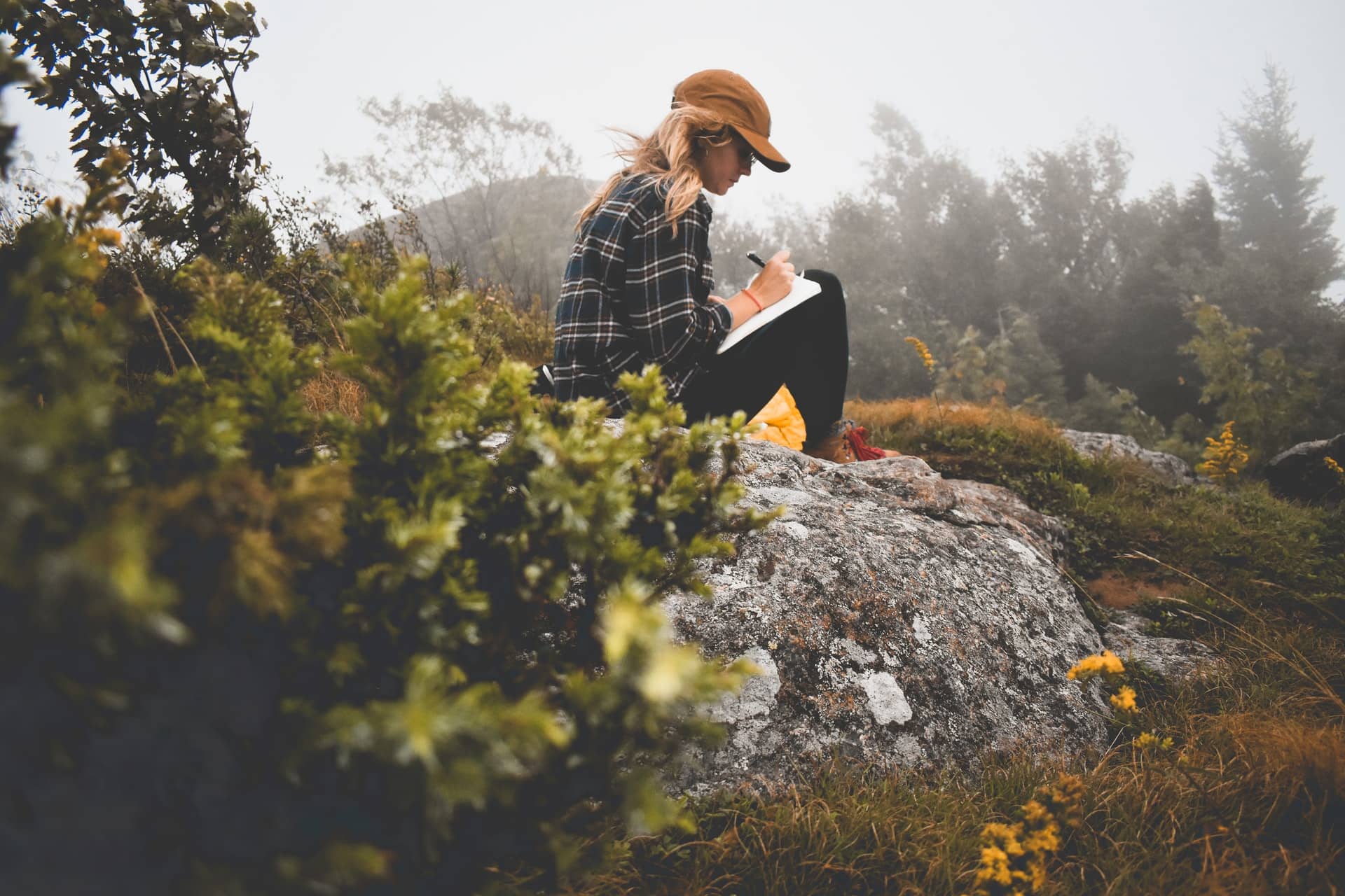 Woman sitting on rock writing in a journal