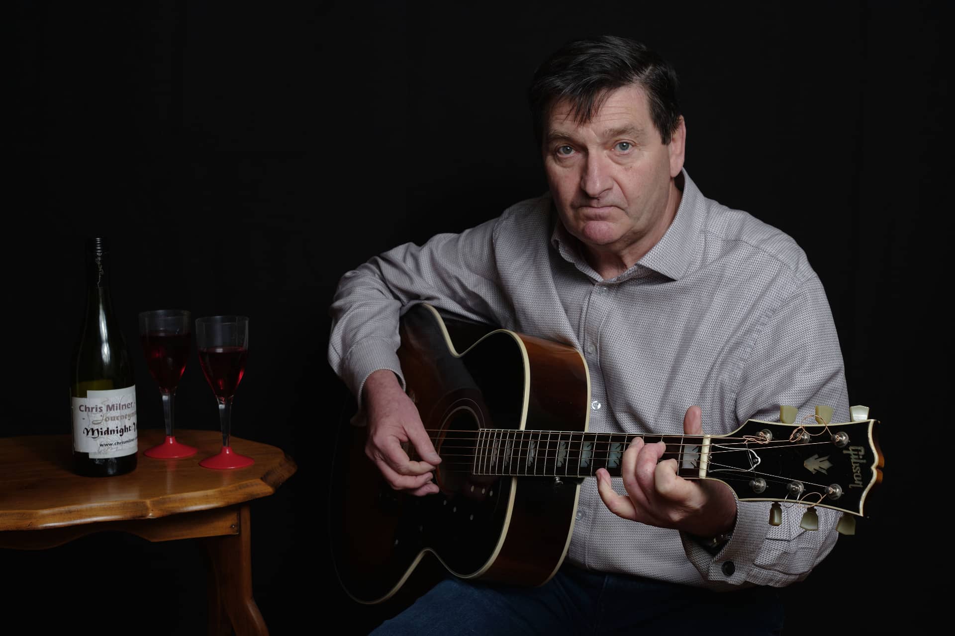 Chris Milner with guitar and bottle of wine with two glasses on table