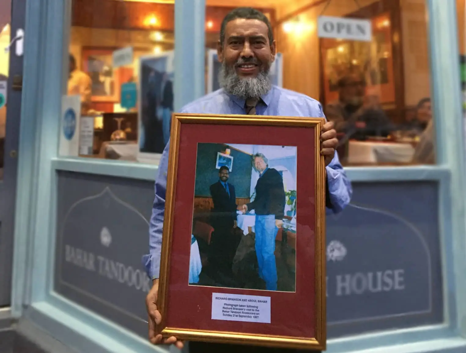 Abdul Bahar outside his restaurant holding the photo of him and Richard Branson from 1997